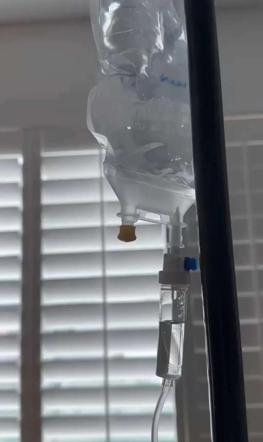 An IV bag and drip chamber in soft window light